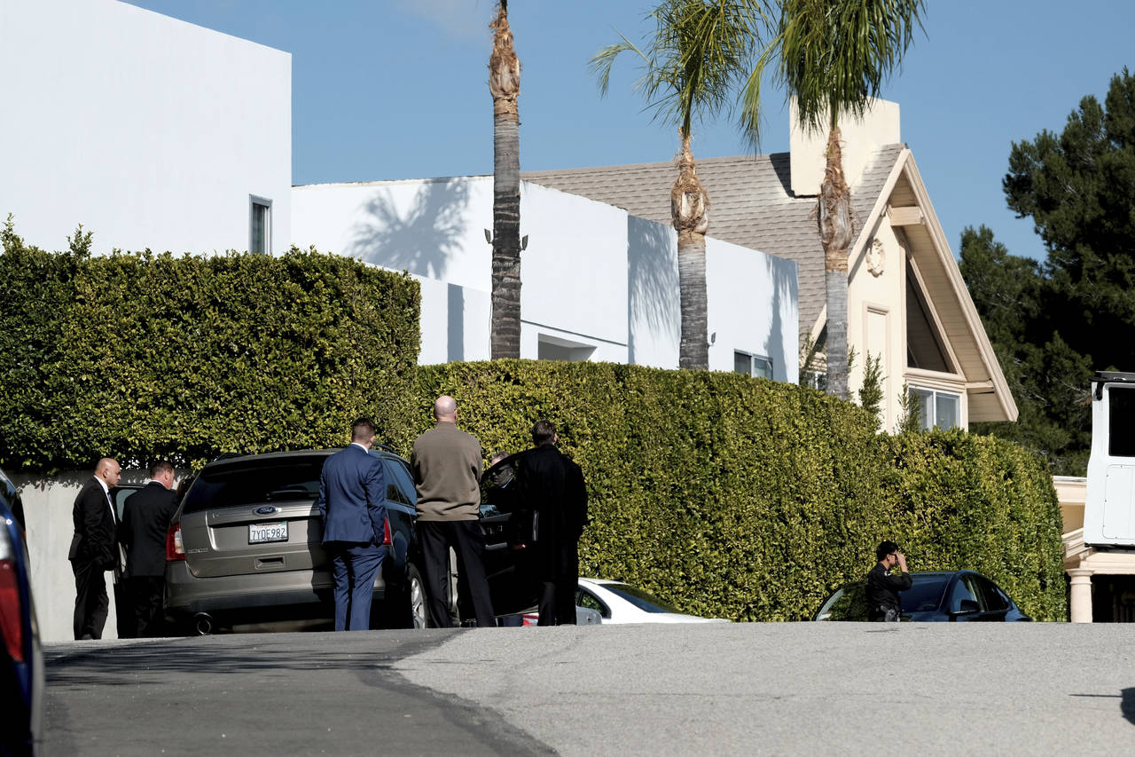Police investigators stand in a street near a house where three people were killed and four others ...