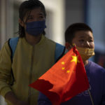
              FILE - A boy wearing a face mask carries a Chinese flag as he walks along a pedestrian shopping street in Beijing on Oct. 6, 2022. China has announced its first overall population decline in recent years amid an aging society and plunging birthrate. (AP Photo/Mark Schiefelbein, File)
            