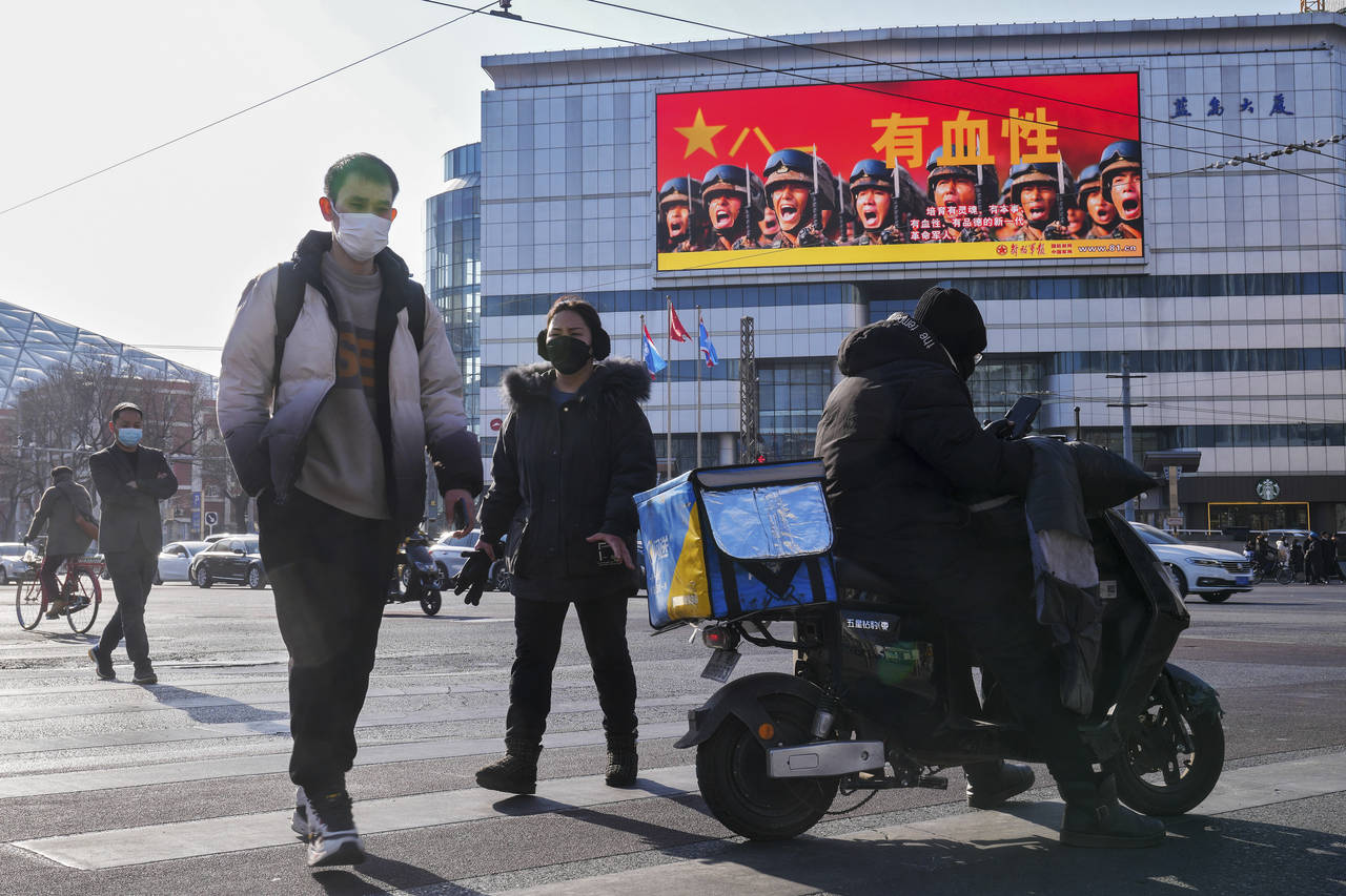 People walk across a street near a large screen promoting the Chinese People's Liberation Army carr...