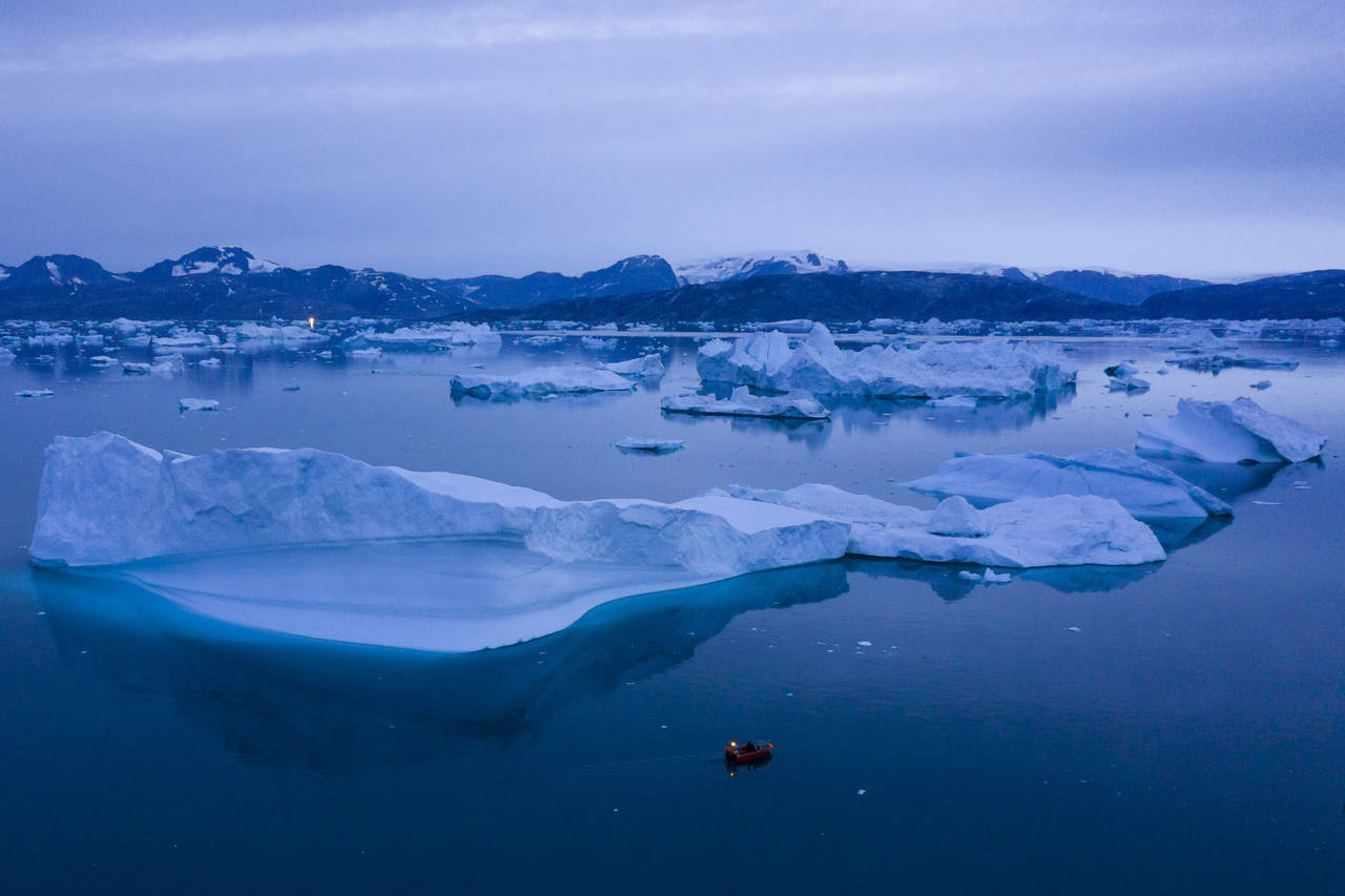 FILE - A boat navigates at night next to large icebergs near the town of Kulusuk, in eastern Greenl...