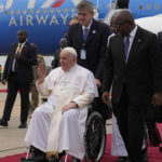 
              Pope Francis on a wheelchair is flanked by Congolese Prime Minister Sama Lukonde, center right, as he arrives in Kinshasa, Democratic Republic of the Congo, Tuesday, Jan. 31, 2023 to start his six-day pastoral visit to Congo and South Sudan where he'll bring a message of peace to countries riven by poverty and conflict. (AP Photo/Gregorio Borgia)
            