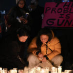 
              Women place candles at a memorial while a man holds a sign during a vigil outside Monterey Park City Hall, blocks from the Star Ballroom Dance Studio on Tuesday, Jan. 24, 2023, in Monterey Park, Calif. A gunman killed multiple people at the ballroom dance studio late Saturday amid Lunar New Years celebrations in the predominantly Asian American community. (AP Photo/Ashley Landis)
            