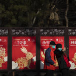 
              Visitors wearing face masks pose in front of a row of Year of the Rabbit themed billboards at a public park in Beijing on the first day of the Lunar New Year holiday, Sunday, Jan. 22, 2023. (AP Photo/Mark Schiefelbein)
            