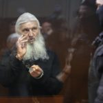 
              Nikolai Romanov, a former monk known as Father Sergiy until he was excommunicated by the Russian Orthodox Church, baptizes those present in the hall from behind a glass cage during his trial in Moscow, Russia, Friday, Jan. 27, 2023. The monk, who denied that the coronavirus existed and challenged the Kremlin, was handed a new prison sentence Friday on charges of inciting hatred. (AP Photo/Alexander Zemlianichenko)
            
