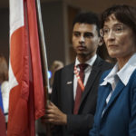 Diplomatic intern Naji Osman, left, holds the Switzerland national flag, as Switzerland's United Nations Ambassador Pascale Baeriswyl, right, prepares for its installation during a ceremony for five newly-elected non-permanent members to serving on the United Nations Security Council for the term 2023-2024, Tuesday Jan. 3, 2023 at U.N. headquarters. (AP Photo/Bebeto Matthews)