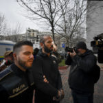 
              Police officers escort Andrew Tate outside the Directorate for Investigating Organized Crime and Terrorism (DIICOT) where prosecutors examine electronic equipment confiscated during the investigation in their case, in Bucharest, Romania, Wednesday, Jan. 25, 2023. Divisive influencer Andrew Tate and his brother Tristan, are held on charges of being part of an organized crime group, human trafficking and rape. (AP Photo/Alexandru Dobre)
            