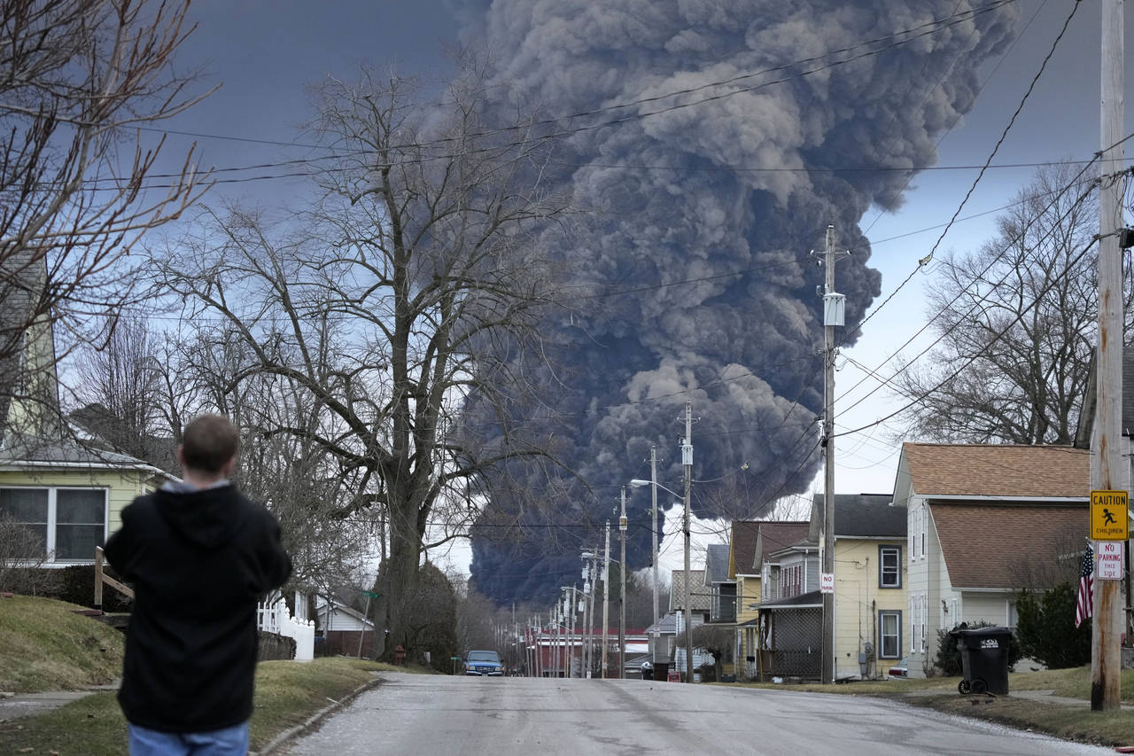 A man takes photos as a black plume rises over East Palestine, Ohio, as a result of a controlled de...
