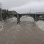 
              The rain-swollen Los Angeles River flows near downtown Los Angeles on Saturday, Feb. 25, 2023, as a powerful storm pounds Southern California. The National Weather Service said periods of heavy rain and mountain snow would continue before winding down by evening. (AP Photo/John Antczak)
            