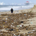 
              A man, dog and two kids walk near a pile of trash and debris on the beach that washed down the Santa Ana River in Huntington Beach on Monday, February 27, 2023, after the recent rain storms that hit Southern California. (Leonard Ortiz/The Orange County Register via AP)
            