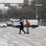
              A pair of pedestrians cross a road as drivers make their way down slush and icy road conditions, Wednesday, Feb. 1, 2023, in Dallas. (AP Photo/Tony Gutierrez)
            