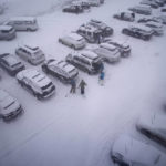 
              People stand in the parking area of the Alpine Base Area at Palisades Tahoe during a winter storm Friday, Feb. 24, 2023, in Alpine Meadows, Calif. California and other parts of the West are facing heavy snow and rain from the latest winter storm to pound the United States. (AP Photo/John Locher)
            
