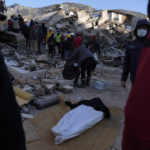 
              People stand around a dead body was taken out from the rubble of a destroyed building in Antakya, southern Turkey, Thursday, Feb. 9, 2023. Tens of thousands of people who lost their homes in a catastrophic earthquake huddled around campfires in the bitter cold and clamored for food and water Thursday, three days after the temblor hit Turkey and Syria. (AP Photo/Khalil Hamra)
            