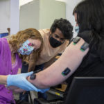 
              In this photo provided by UPMC and Pitt Health Sciences, occupational therapist Amy Boos, left, and Carnegie Mellon graduate student Nikhil Verma connect sensors on the arm of research participant Heather Rendulic in Pittsburgh on May 19, 2021. A stroke left Rendulic with little use of her left hand and arm, so she volunteered for a first-of-its-kind experiment that stimulates her spinal cord in spots that control upper limb motion. (Tim Betler/UPMC and Pitt Health Sciences via AP)
            