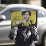 
              A supporter of former Justice Minister Cho Kuk holds a sign with a picture of Cho Kuk outside of the Seoul Central District Court in Seoul, South Korea, Friday, Feb. 3, 2023. The court on Friday sentenced Cho to two years in prison, after he was found guilty of creating fake credentials to help his children get into prestigious schools, a scandal that rocked the country’s previous government and sparked huge protests. The letters read "Reform the Prosecution," and "Protect Cho Kuk." (AP Photo/Lee Jin-man)
            