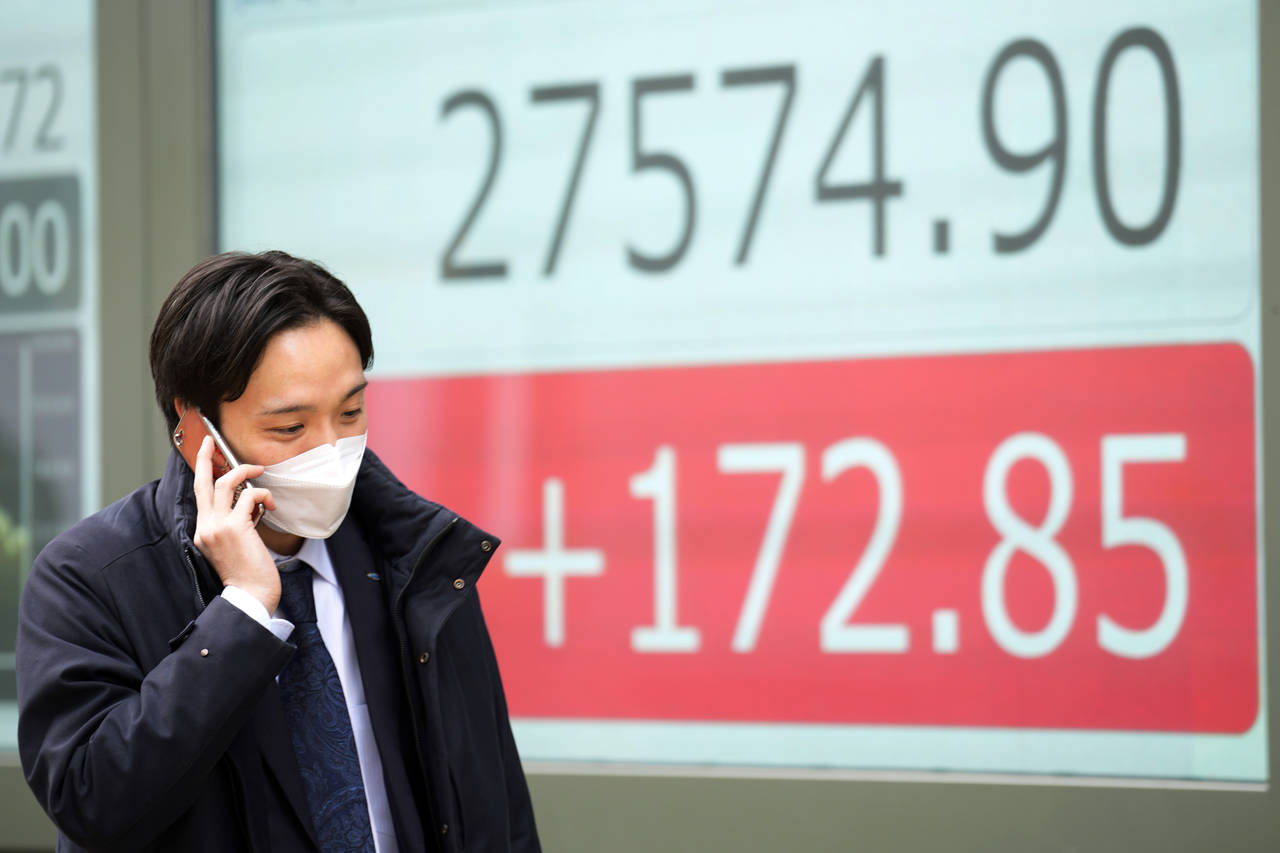 A person wearing a protective mask walks in front of an electronic stock board showing Japan's Nikk...
