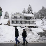 
              Two residents walk past the piles of snow in Running Springs, Calif., Tuesday, Feb. 28, 2023. Beleaguered Californians got hit again Tuesday as a new winter storm moved into the already drenched and snow-plastered state, with blizzard warnings blanketing the Sierra Nevada and forecasters warning residents that any travel was dangerous. (AP Photo/Jae C. Hong)
            
