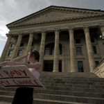 
              FILE - Zoe Schell, from Topeka, Kan., stands on the steps of the Kansas Statehouse during a rally to protest the Supreme Court's ruling on abortion June 24, 2022, in Topeka. Republicans and their anti-abortion allies, who suffered a series of defeats in ballot questions in states across the political spectrum in 2022, are changing tactics as new 2023 legislative sessions and the new election season start. (AP Photo/Charlie Riedel, File)
            