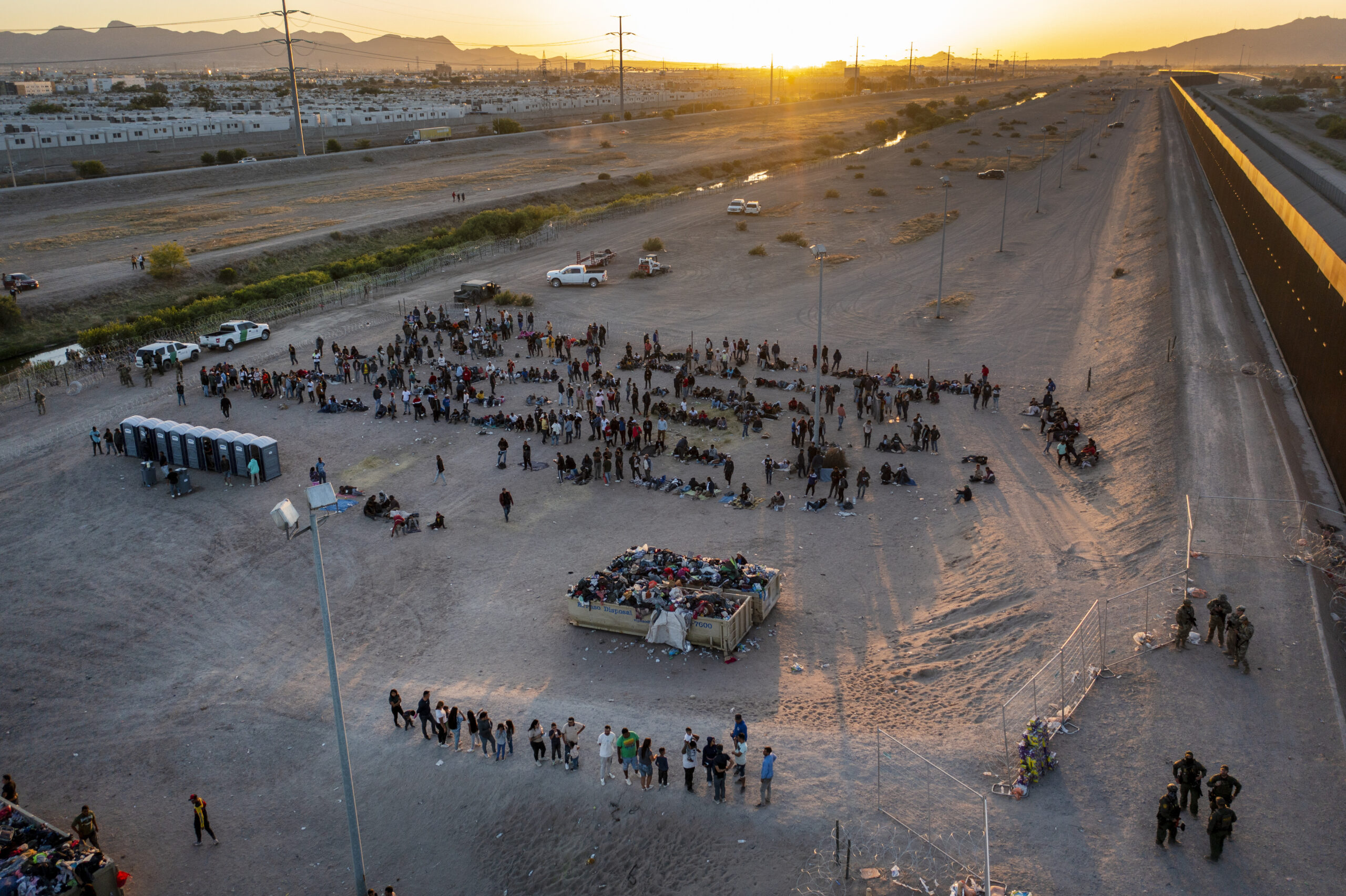 As the sun sets, migrants wait outside a gate in the border fence to enter into El Paso, Texas, to ...