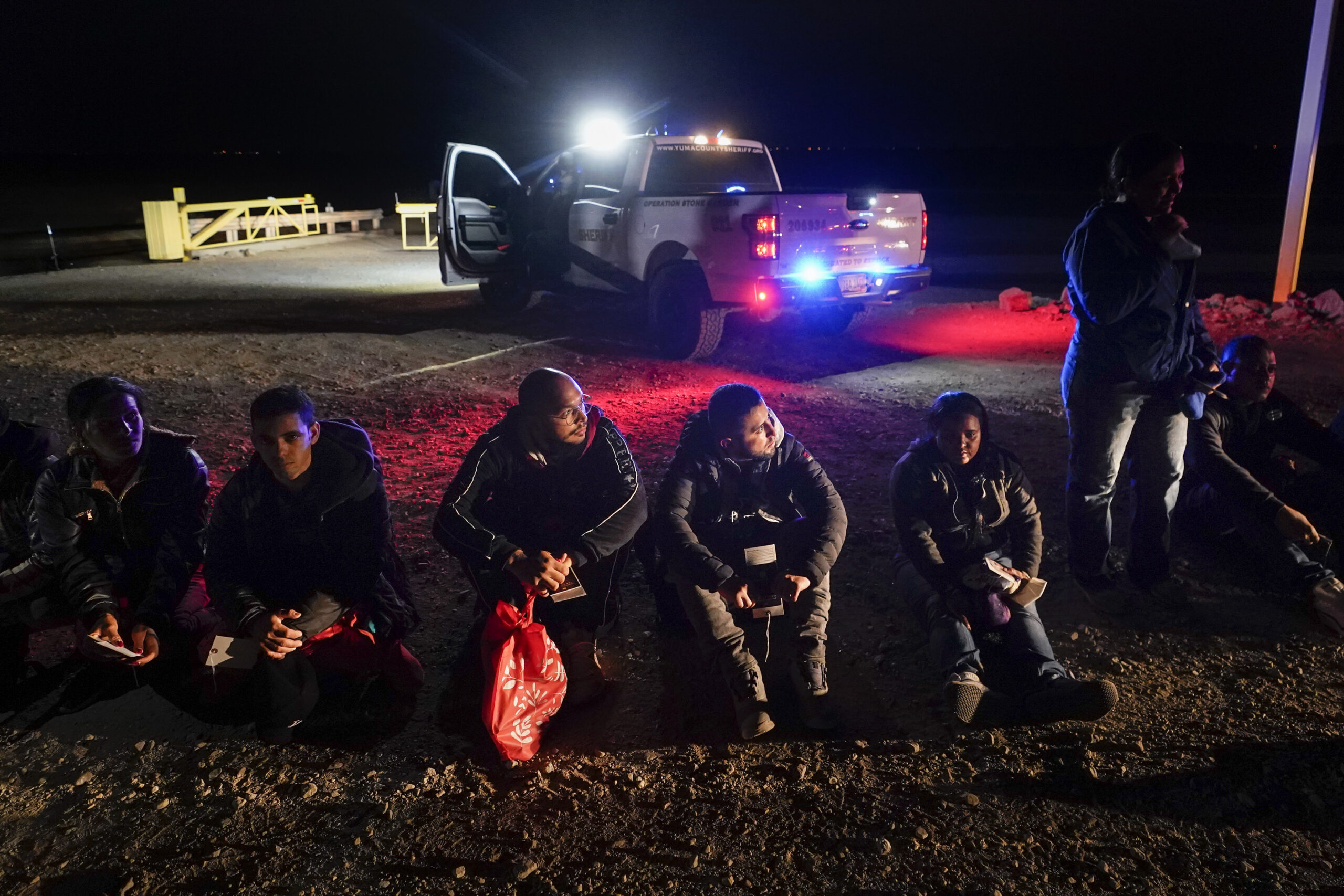 FILE - Migrants wait to be processed after crossing the border, Jan. 6, 2023, near Yuma, Ariz. Doze...