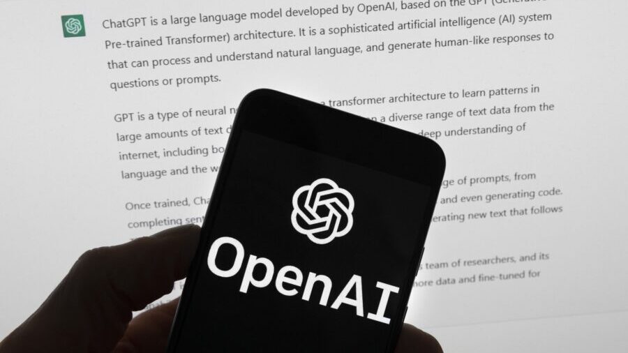 Photo: The OpenAI logo is seen on a mobile phone in front of a computer screen which displays outpu...