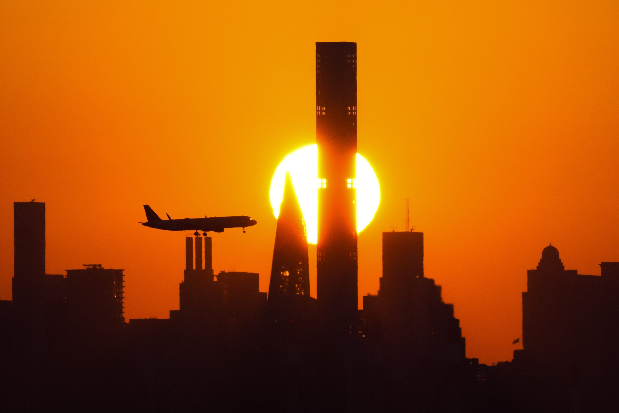 File - The sun sets behind the Manhattan skyline as plane approaches LaGuardia Airport on Sept. 6, ...