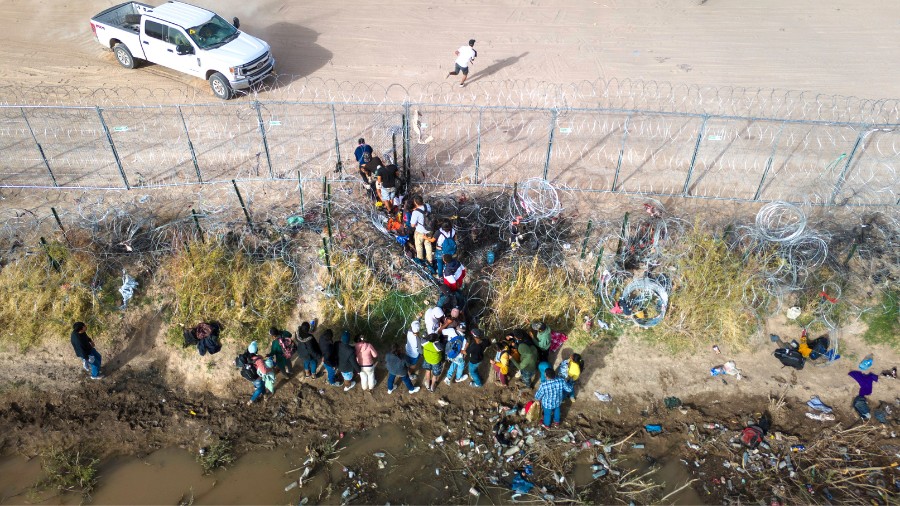 Image: In an aerial view, immigrants pass through coils of razor wire while crossing the U.S.-Mexic...