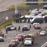 Image:A tow truck removes one of the cars blocking the expressway leading to Seattle-Tacoma International Airport on Monday, April 15, 2024 as people walk by with suitcases toward the airport. A pro-Palestinian protest closed the road to the airport