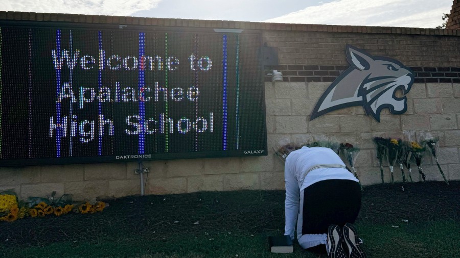 Image: A person kneels in front of flowers that are placed outside the entrance to Apalachee High S...