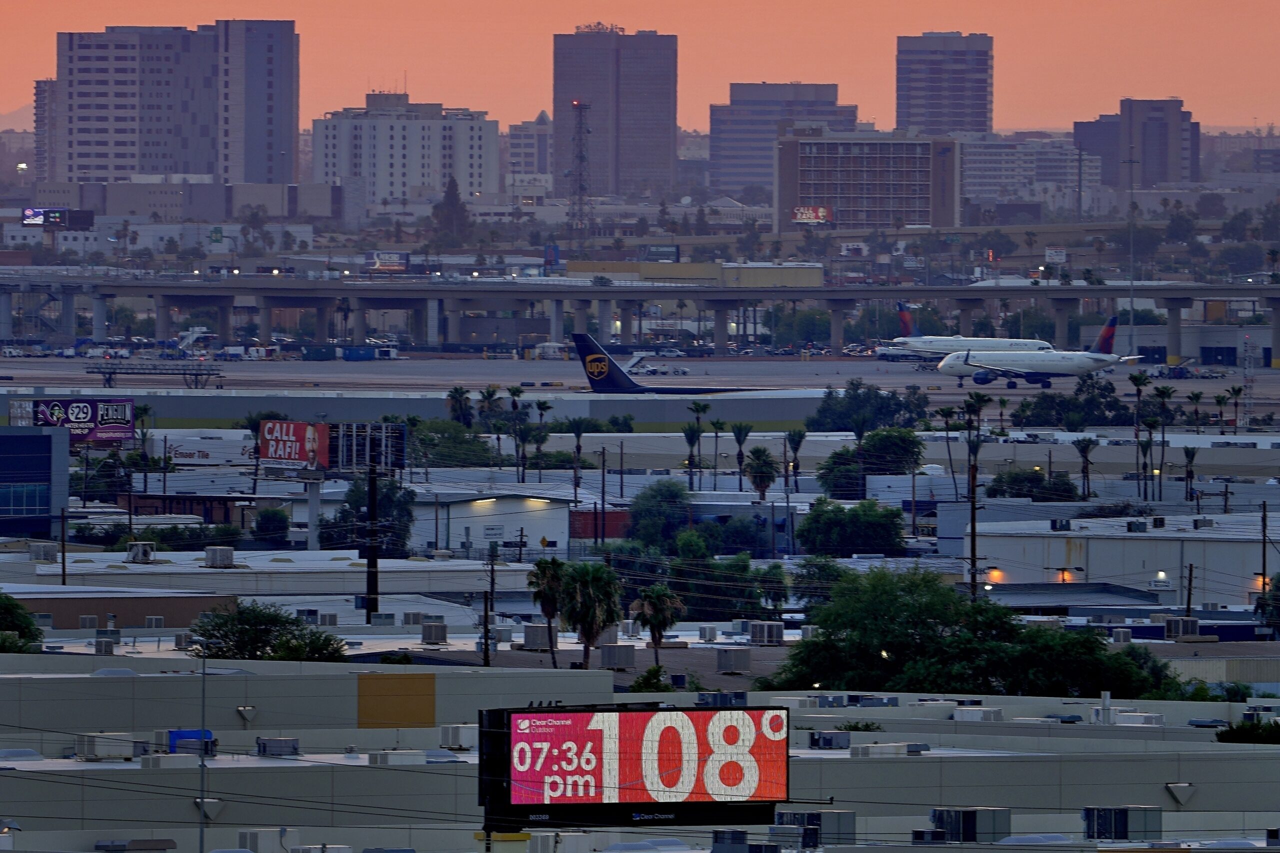 FILE - A sign displays an unofficial temperature as jets taxi at Sky Harbor International Airport a...