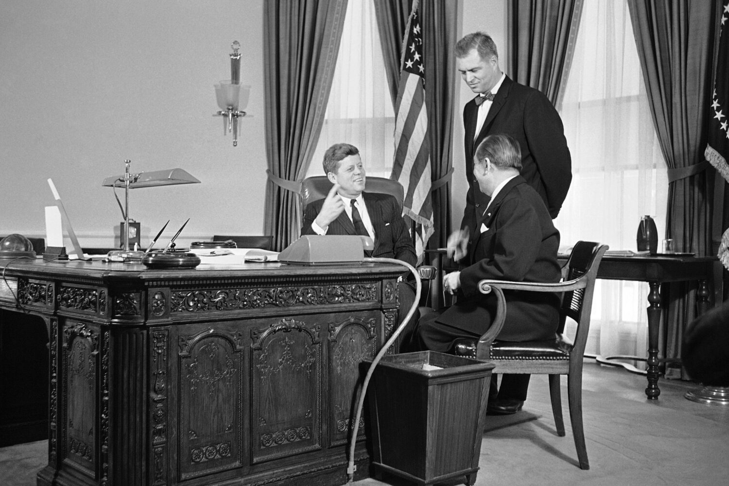 FILE - President John F. Kennedy gestures from behind a richly carved desk, made from the timbers o...