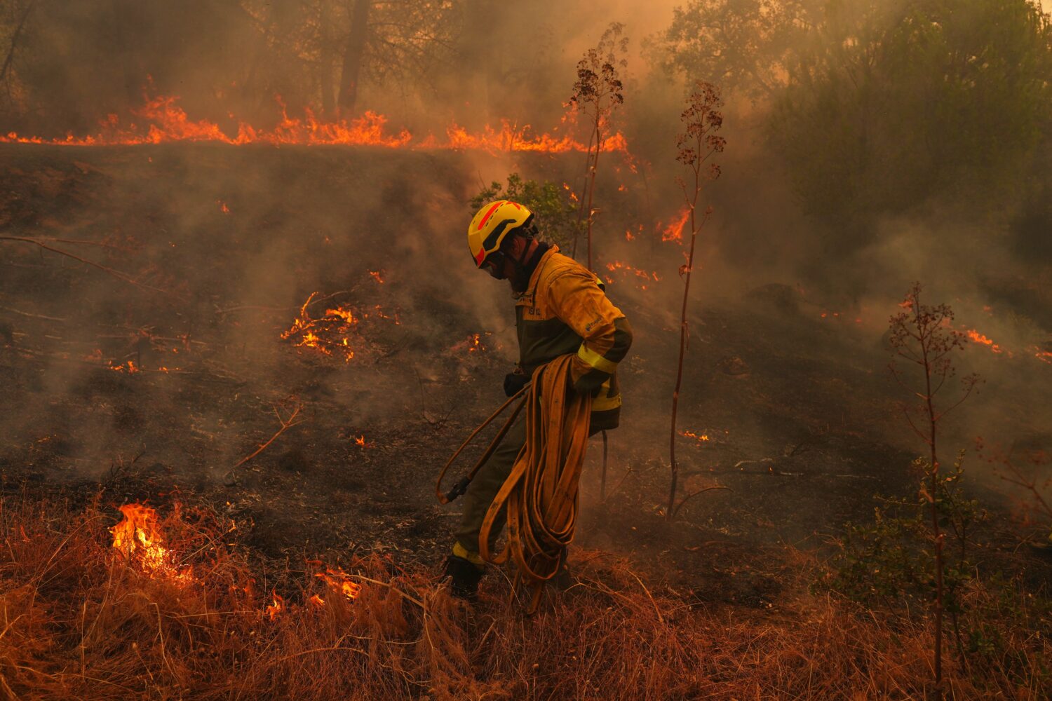 FILE - A firefighter carries a hose while battling a wildfire in San Martin de Valdeiglesias, west ...