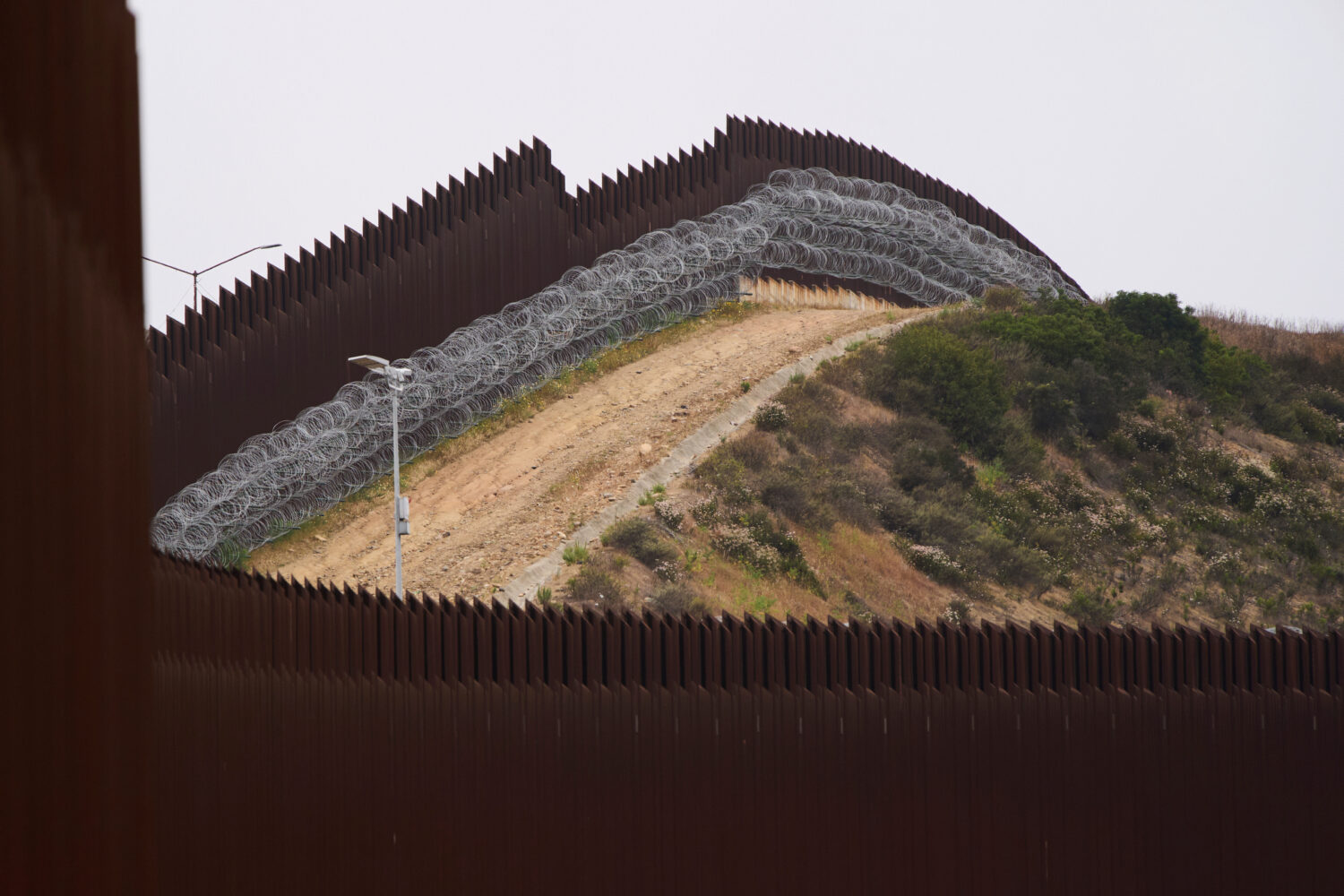 FILE - Concertina wire lines the interior of a border wall separating Tijuana, Mexico, from the Uni...
