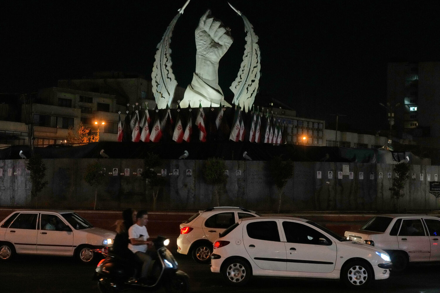 Vehicles drive past a monument depicting the clenched fist of the late Iranian Supreme Leader Ayato...