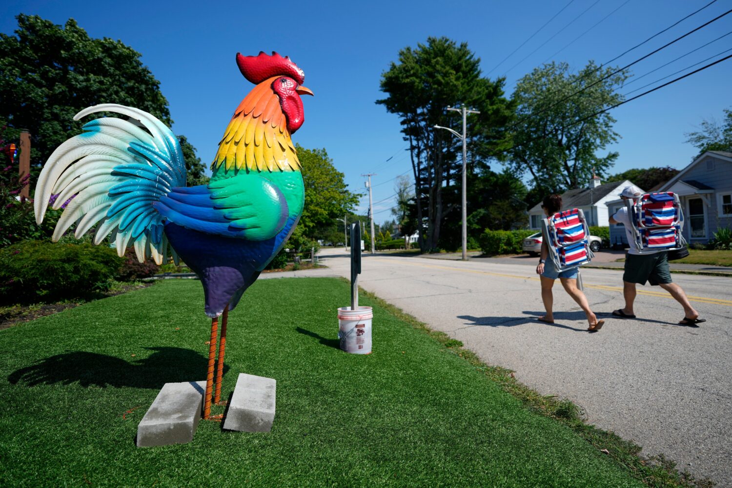Beach-goers pass by a large tin rooster set up outside a motel in solidarity with a young girl with...