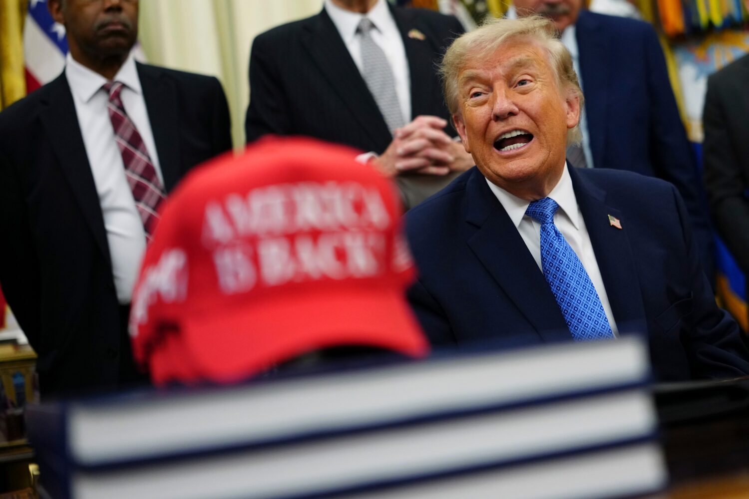 President Donald Trump speaks alongside a red cap stating "America Is Back!" in the Oval Office of ...