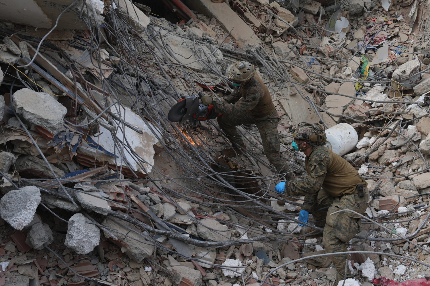 U.S. troops cut through rebar while clearing rubble during a search at a building that collapsed in...