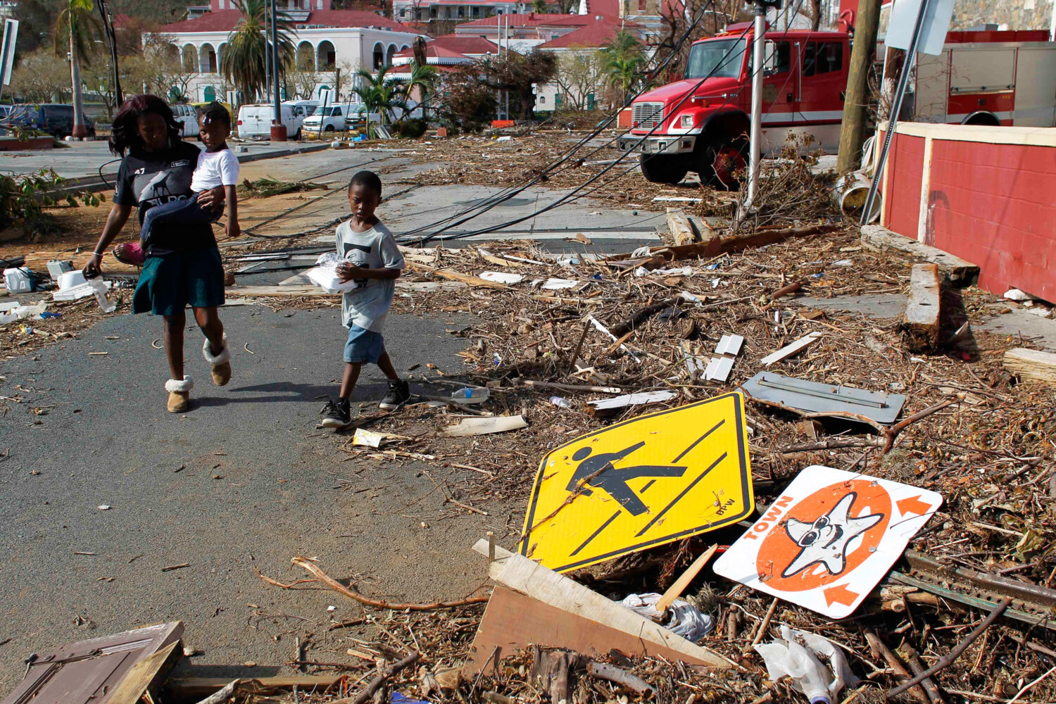 FILE - A woman and her children walk past debris left by Hurricane Irma in Charlotte Amalie, St. Th...