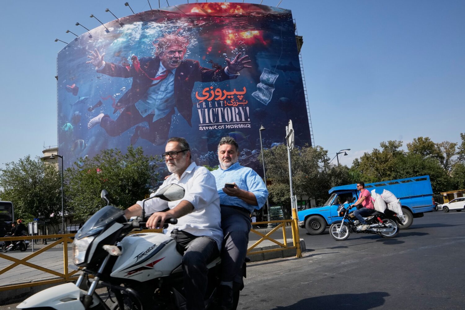 Motorcyclists pass a billboard depicting U.S. President Donald Trump underwater amid explosions, wi...