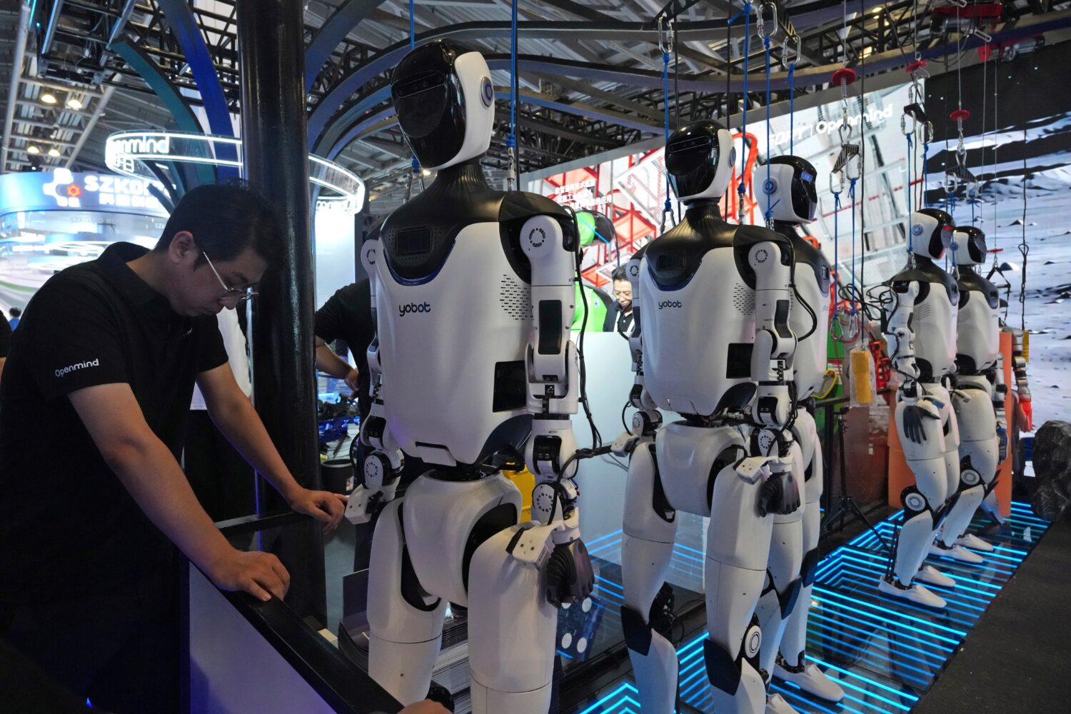 FILE - A worker reacts near a line of humanoid robots displayed at the World AI Conference in Shang...
