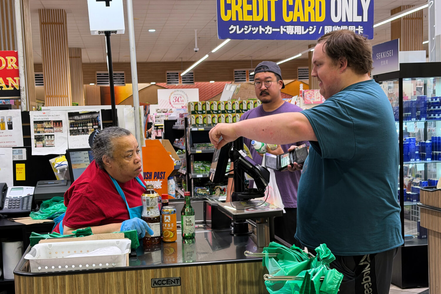 An employee checks a customer's identification card before checking out alcohol at a cash register ...
