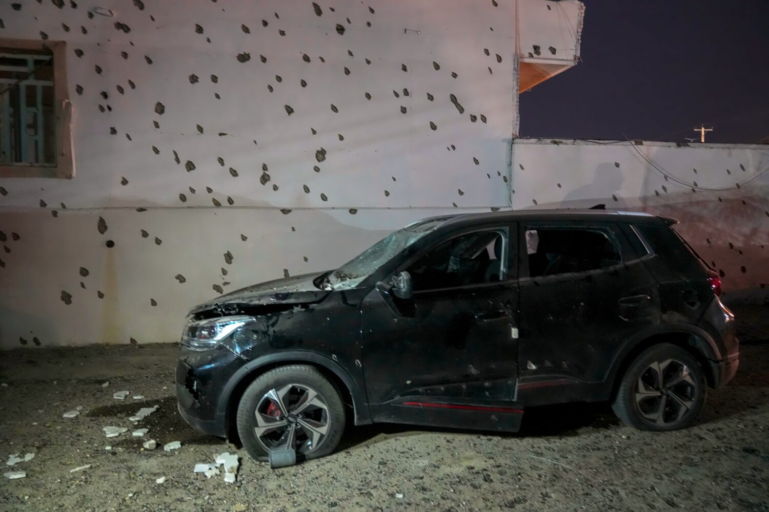 A damaged car sits beside a wall bearing numerous impact marks near the site of a strike in Lamerd,...