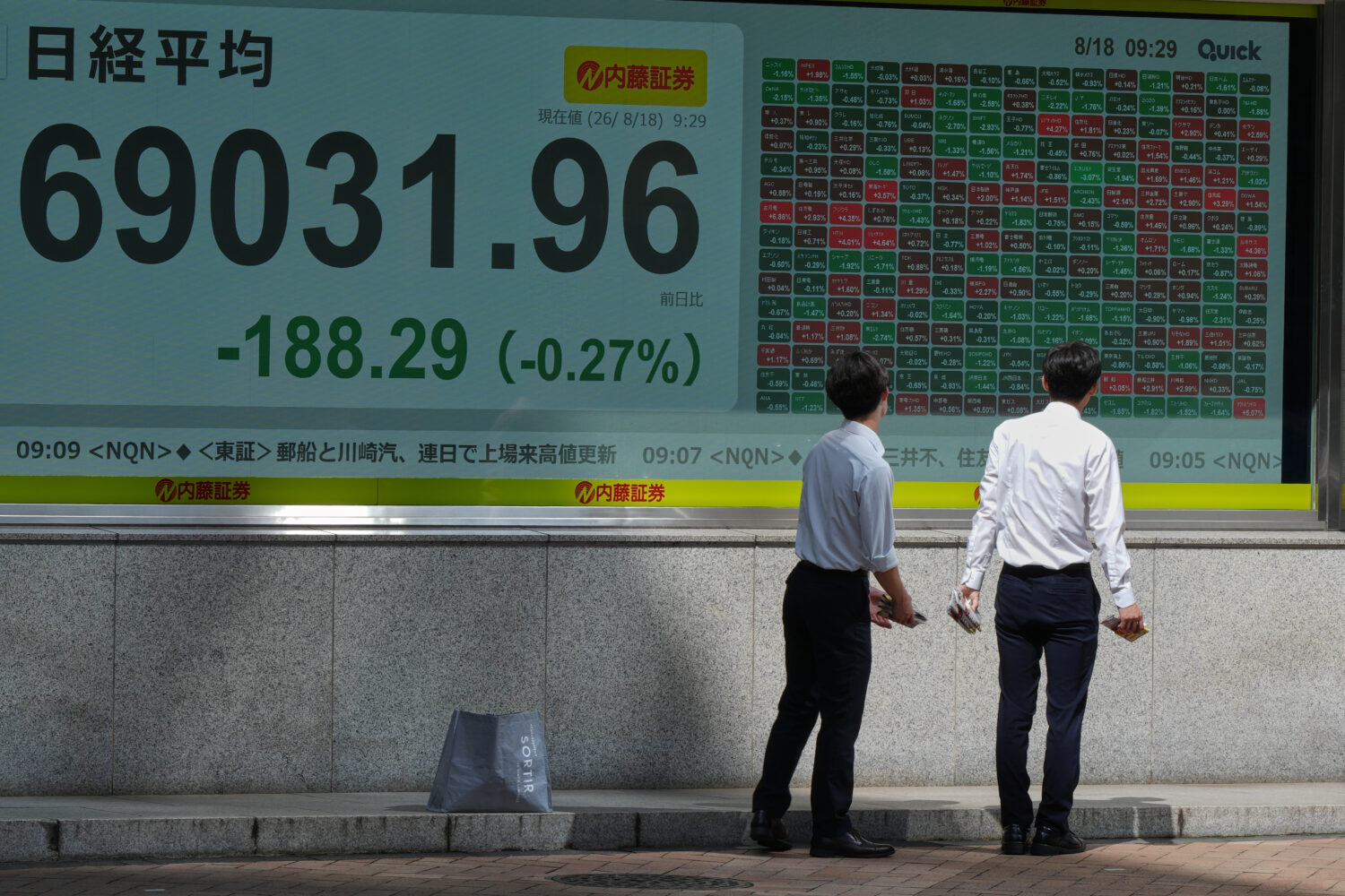 People look at an electronic stock chart board showing Japan's Nikkei index at a securities firm Tu...