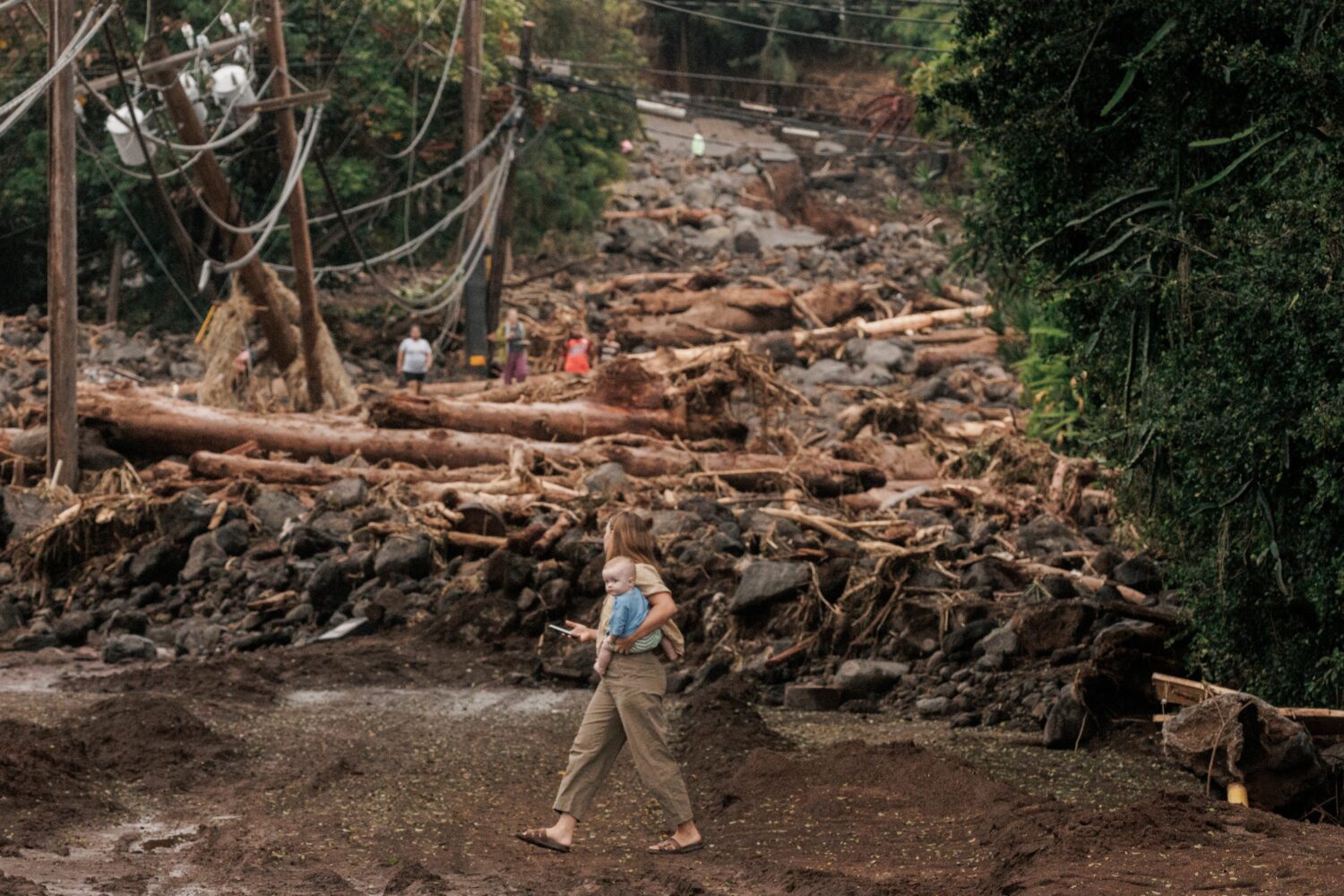 A woman and child walk past a debris-strewn street in Naalehu, Hawaii, Monday, Aug. 17, 2026, after...