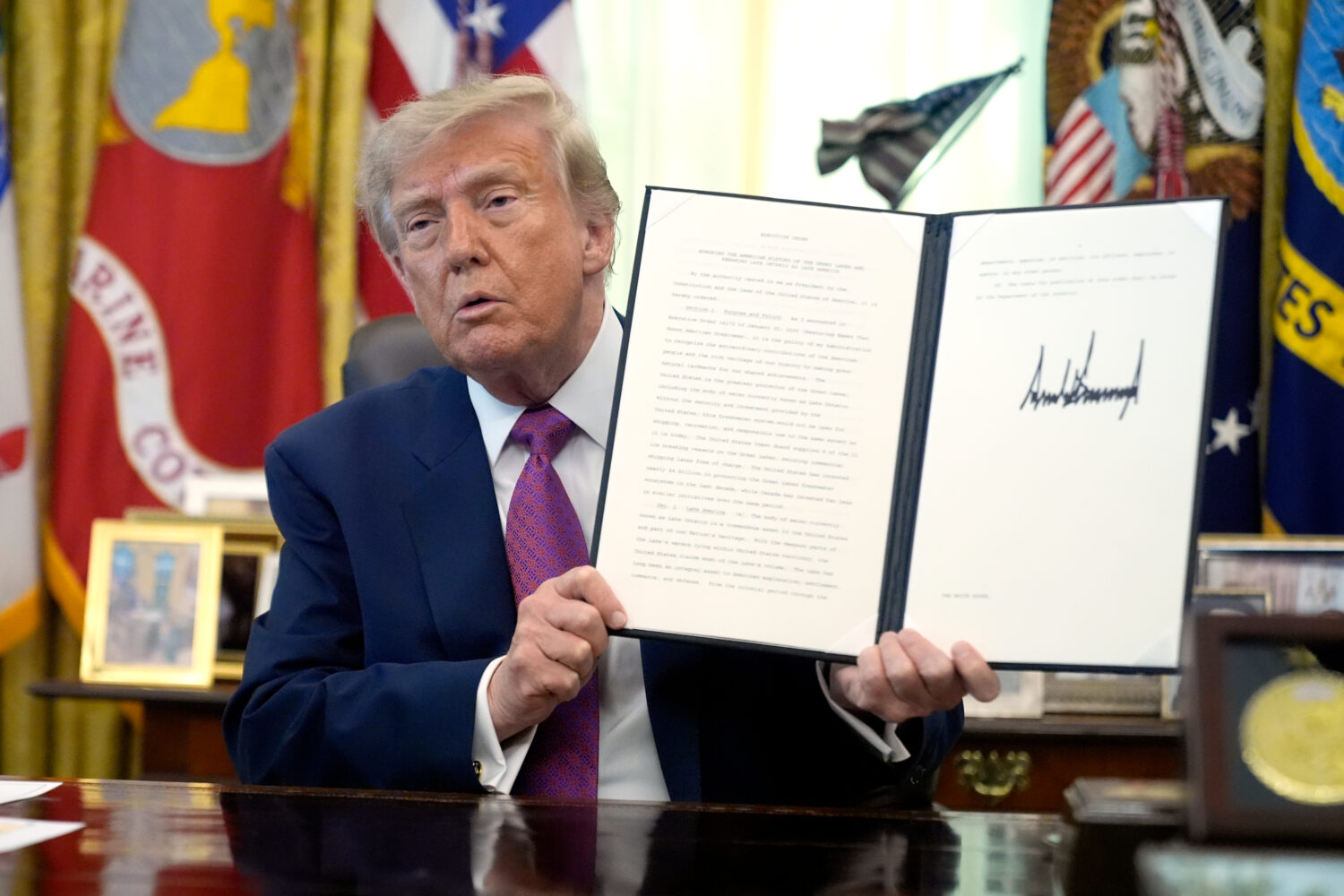 President Donald Trump holds up a signed executive order in the Oval Office of the White House, Thu...