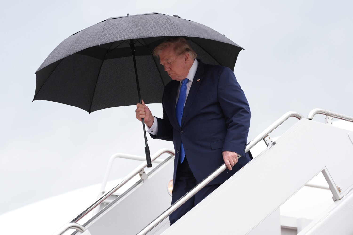 President Donald Trump carries an umbrella as he exits Air Force One at Joint Base Andrews, Md., Su...