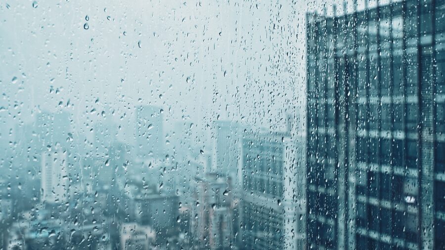 Rain streaks the glass of a window overlooking a gray city. (Photo: Dmitry_Rukhlenko via Envato)...