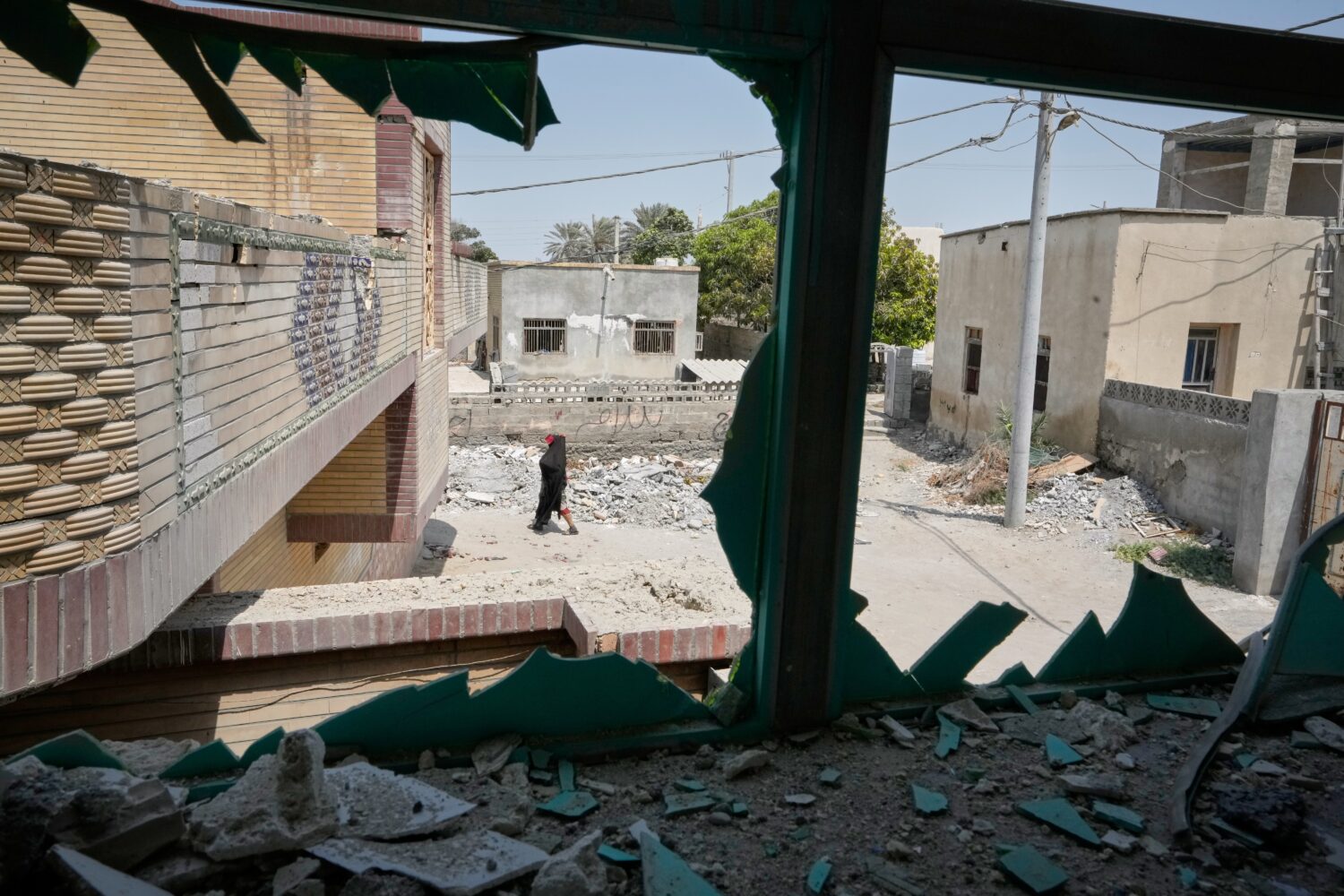 A person walks past debris, seen through a shattered window at the site of what Iranian media said ...