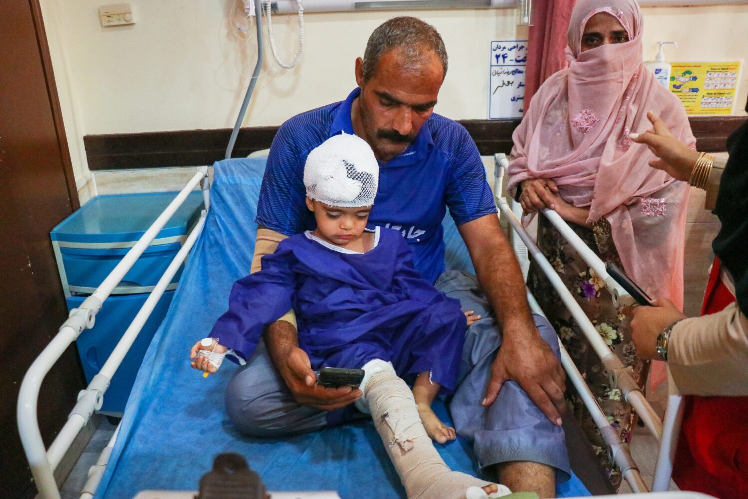 A man sits with a child injured, according to Iranian media, in a strike on a home where a wedding ...