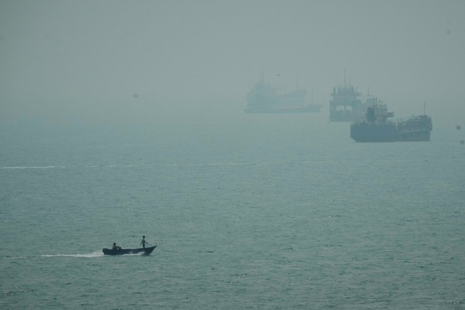 A motorboat travels past commercial vessels anchored amid haze in the Strait of Hormuz off Bandar A...