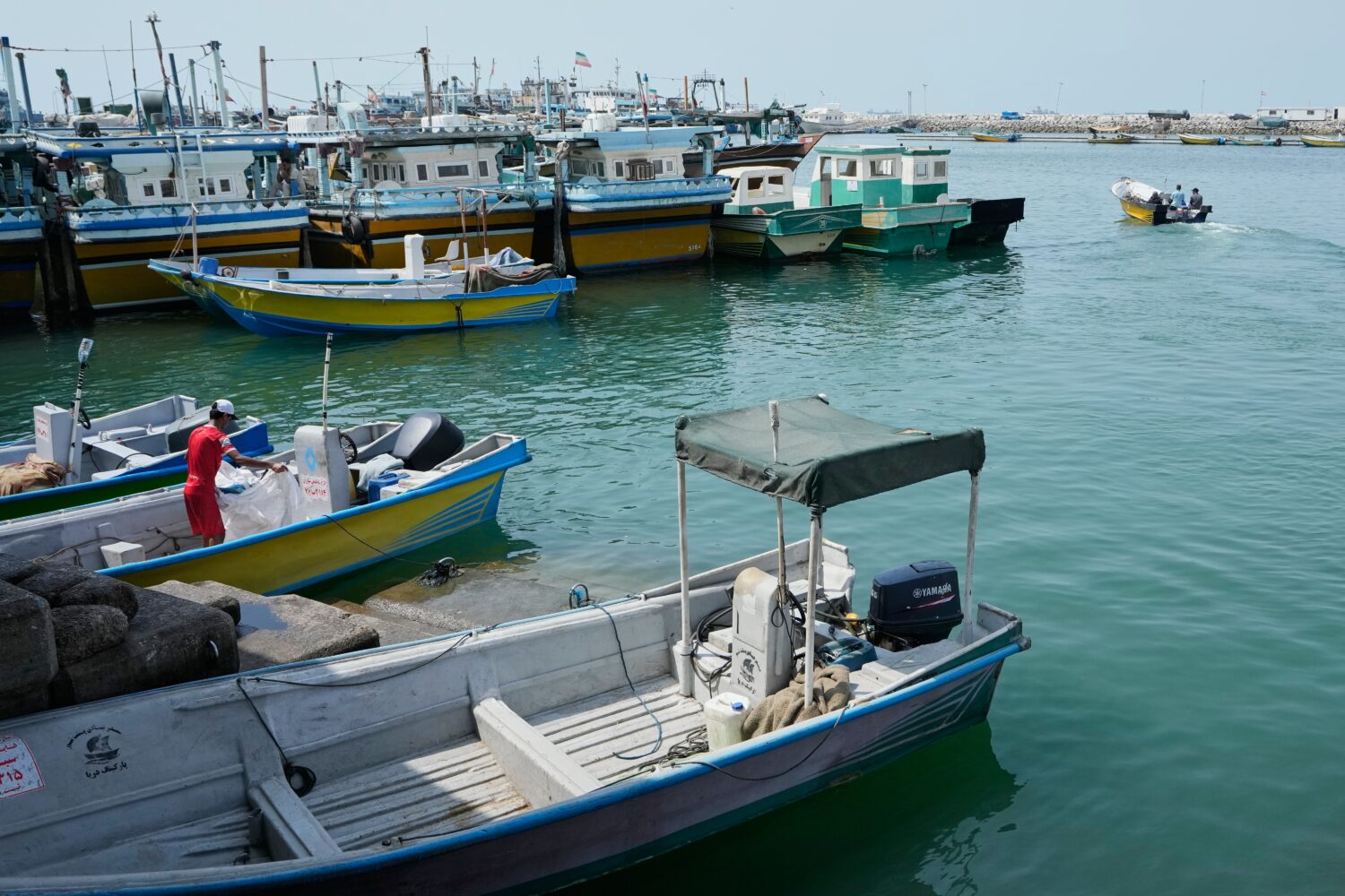 A man works aboard a boat as a motorboat leaves a harbor in Bandar Abbas, Iran, Sunday, Sept. 6, 20...